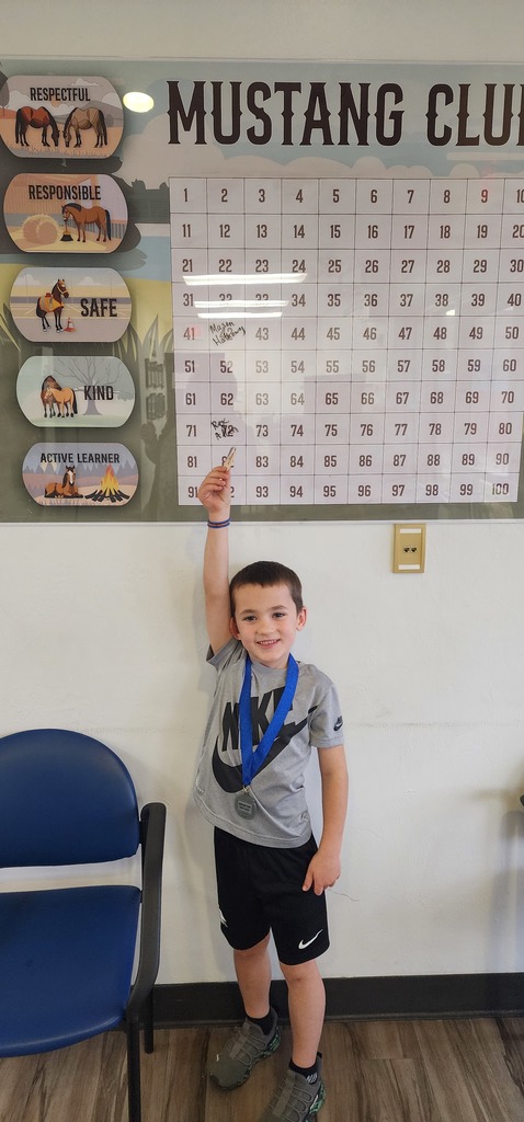 Picture of male student pointing at the Mustang Club board with his medal.