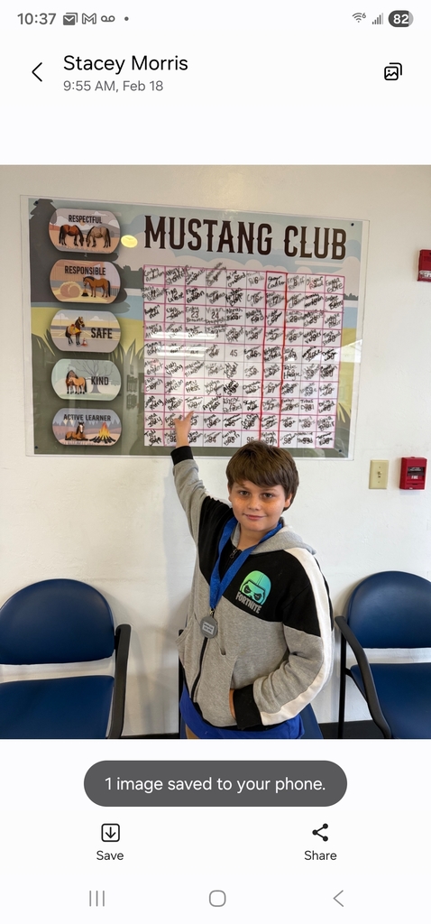 Picture of male student pointing at the Mustang Club board with his medal.