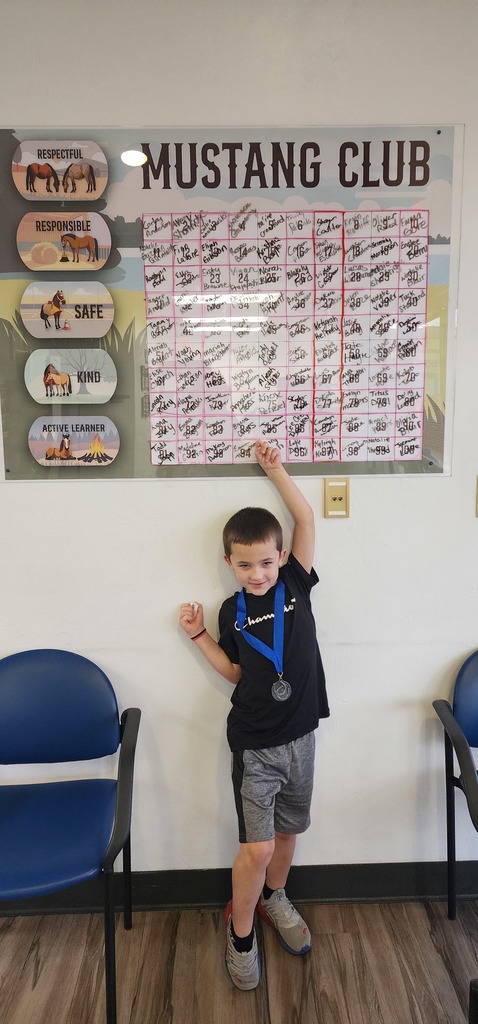 Picture of male student pointing at the Mustang Club board with his medal.