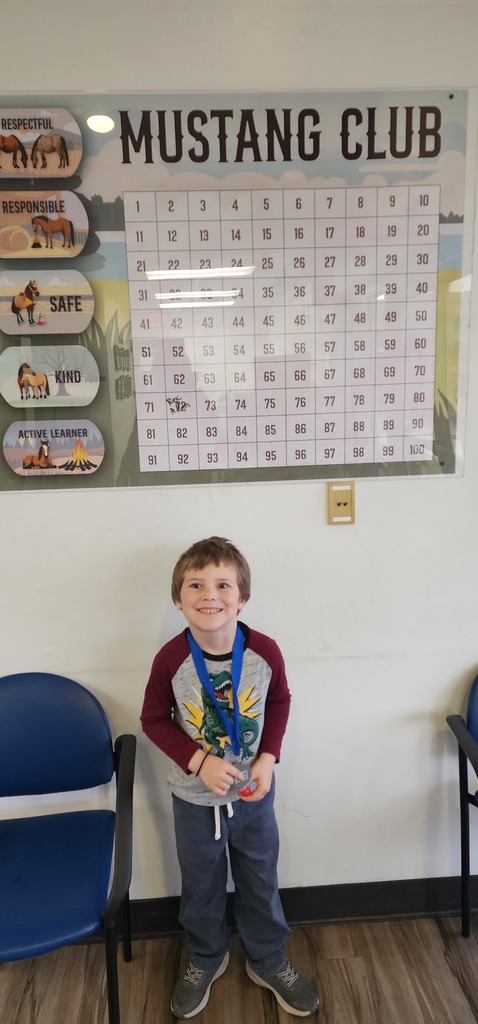 Picture of male student pointing at the Mustang Club board with his medal.