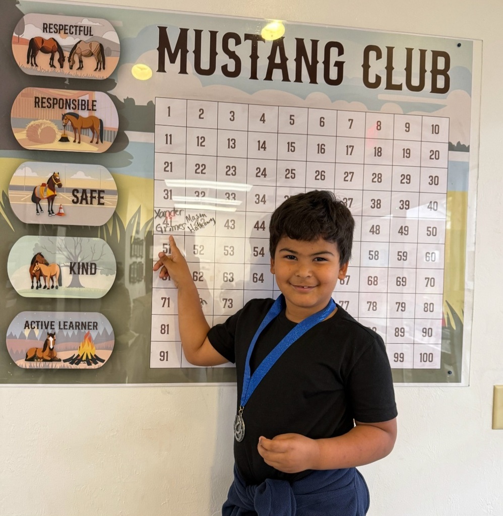 Picture of male student pointing at the Mustang Club board with his medal.