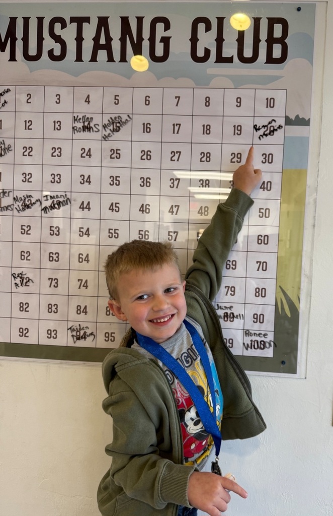 Picture of male student pointing at the Mustang Club board with his medal.