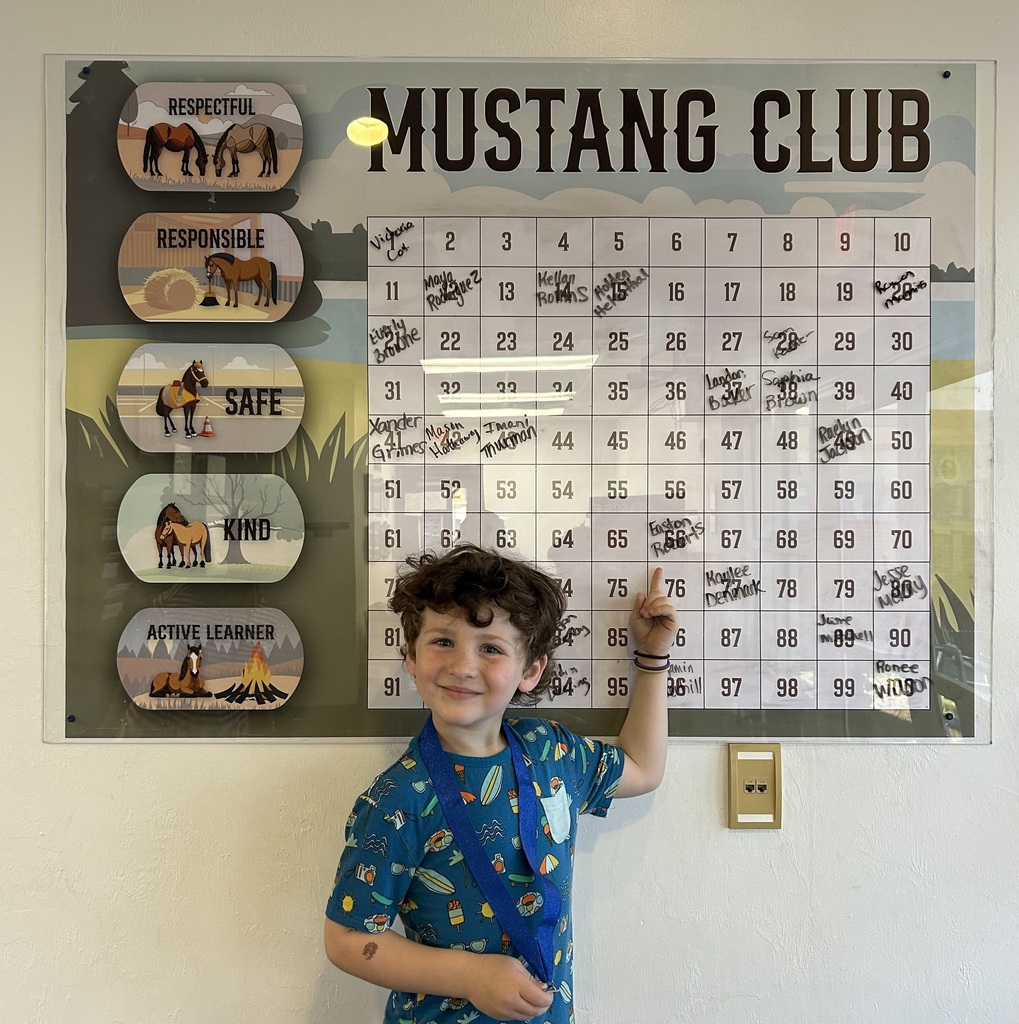 Picture of male student pointing at the Mustang Club board with his medal.
