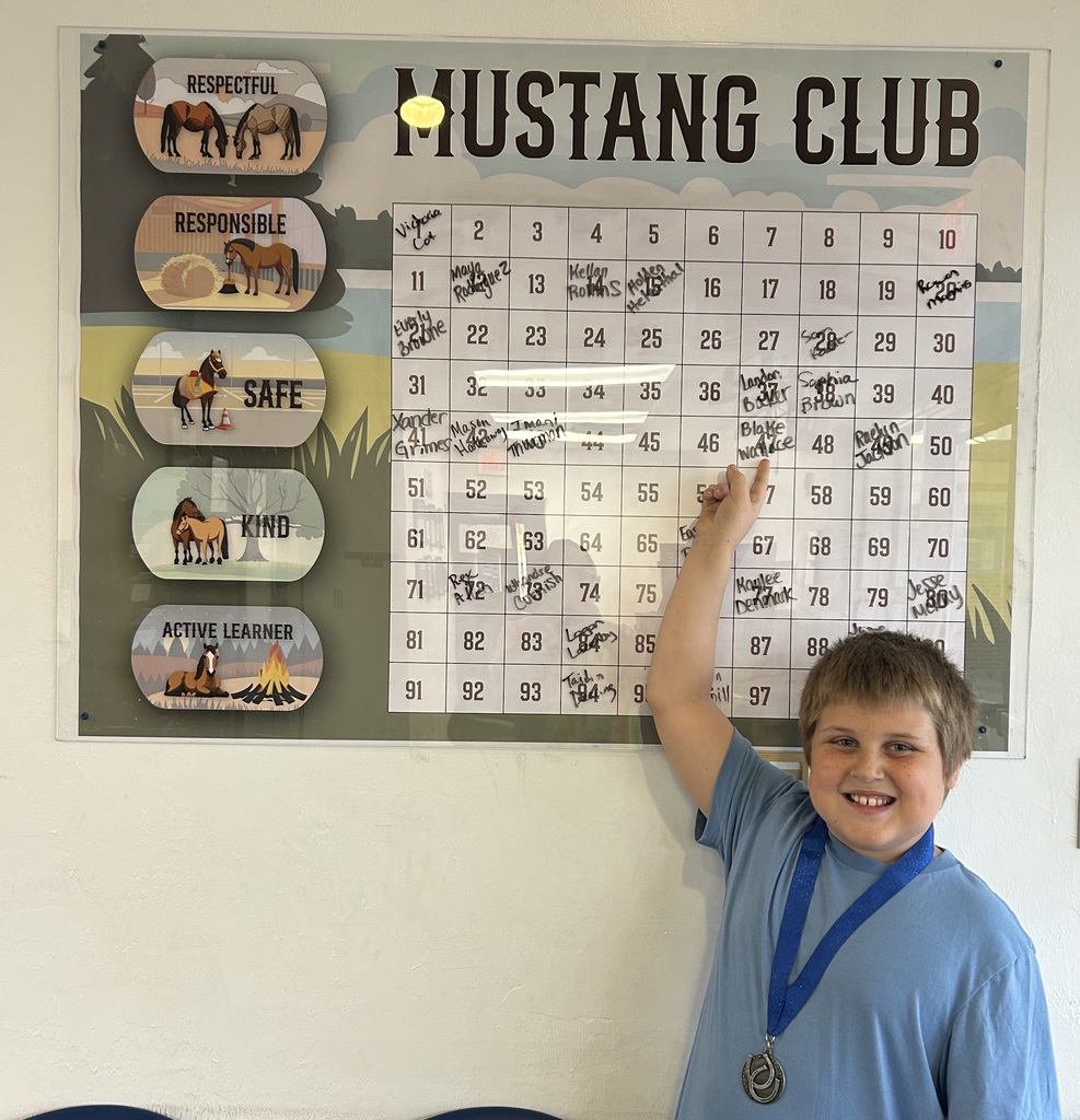 Picture of male student pointing at the Mustang Club board with his medal.