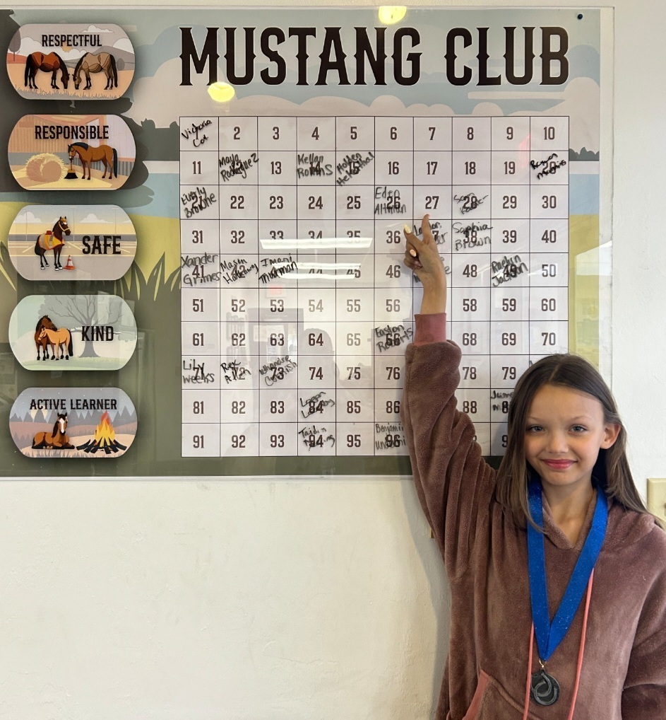 Picture of female student pointing at Mustang Club board 