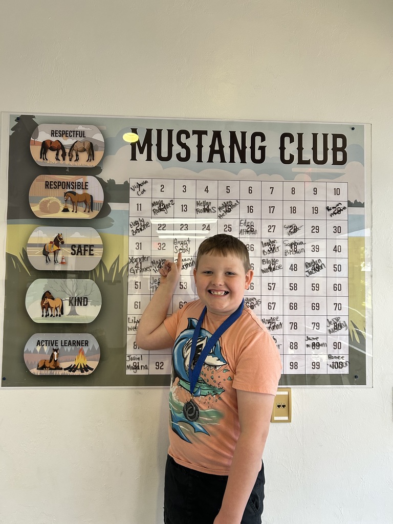 Picture of male student pointing at the Mustang Club board with his medal.