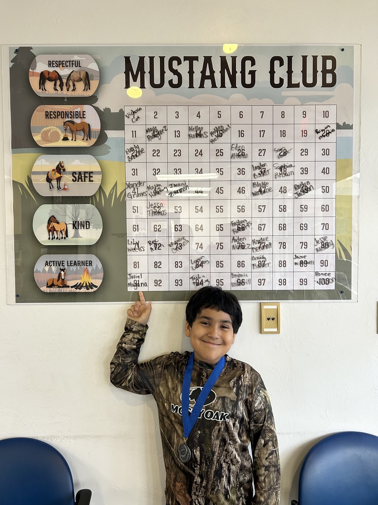 Picture of male student pointing at the Mustang Club board with his medal.