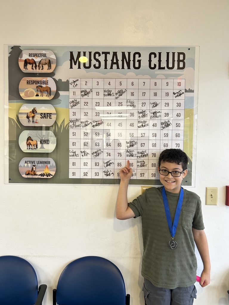 Picture of male student pointing at the Mustang Club board with his medal.