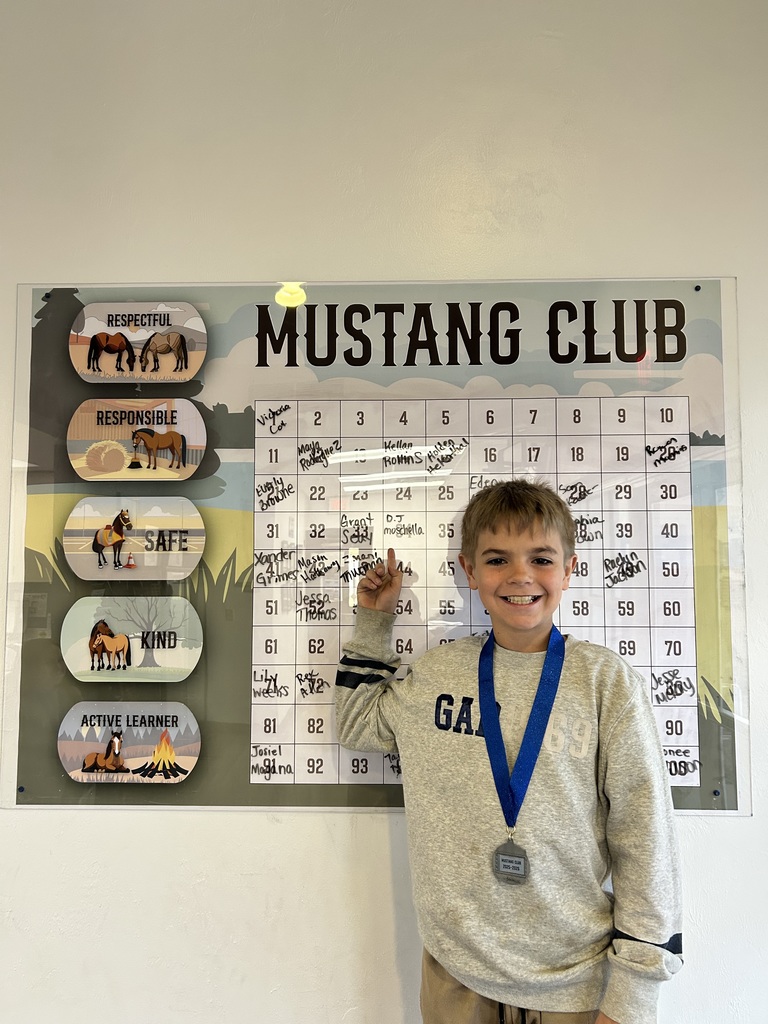 Picture of male student pointing at the Mustang Club board with his medal.