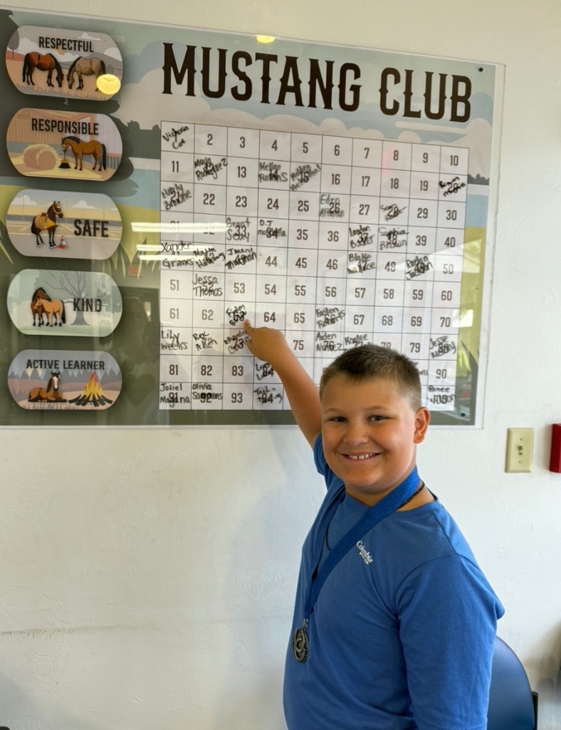 Picture of male student pointing at the Mustang Club board with his medal.