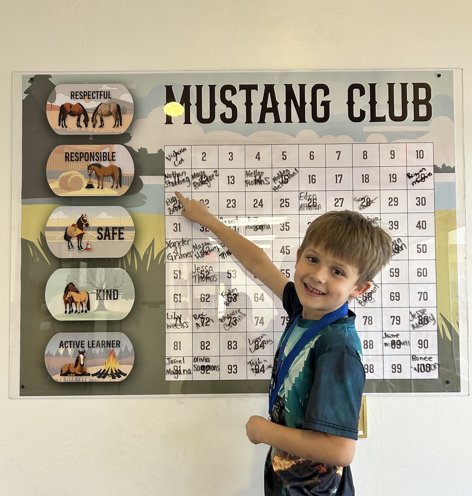 Picture of male student pointing at the Mustang Club board with his medal.