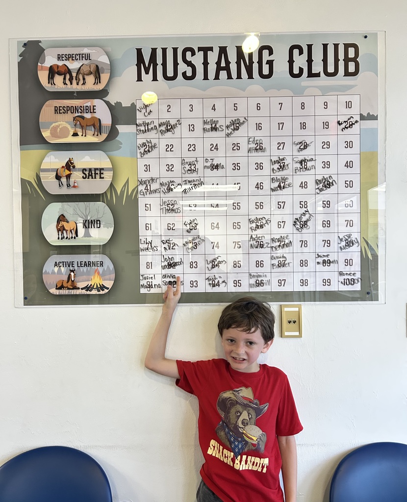 Picture of male student pointing at the Mustang Club board with his medal.
