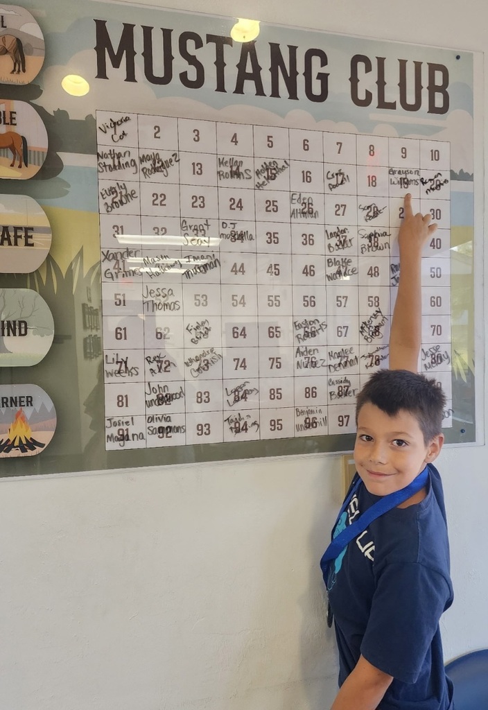 Picture of male student pointing at the Mustang Club board with his medal.