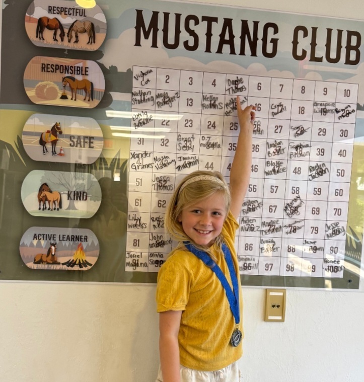 Picture of female student pointing at the Mustang Club board.