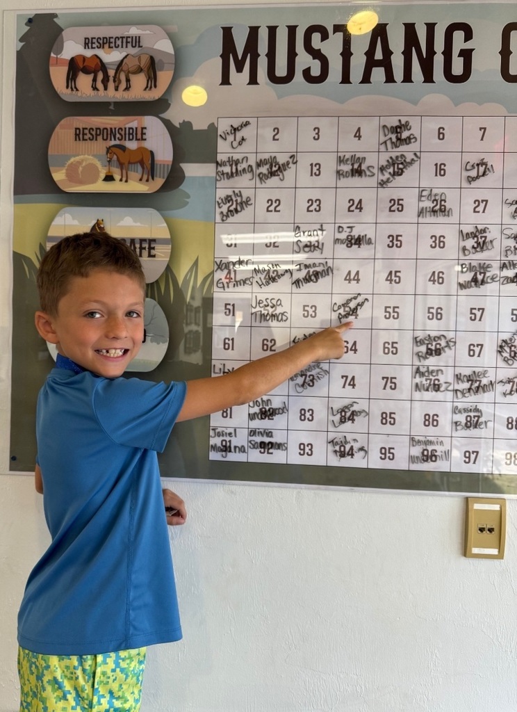 Picture of male student pointing at the Mustang Club board with his medal.