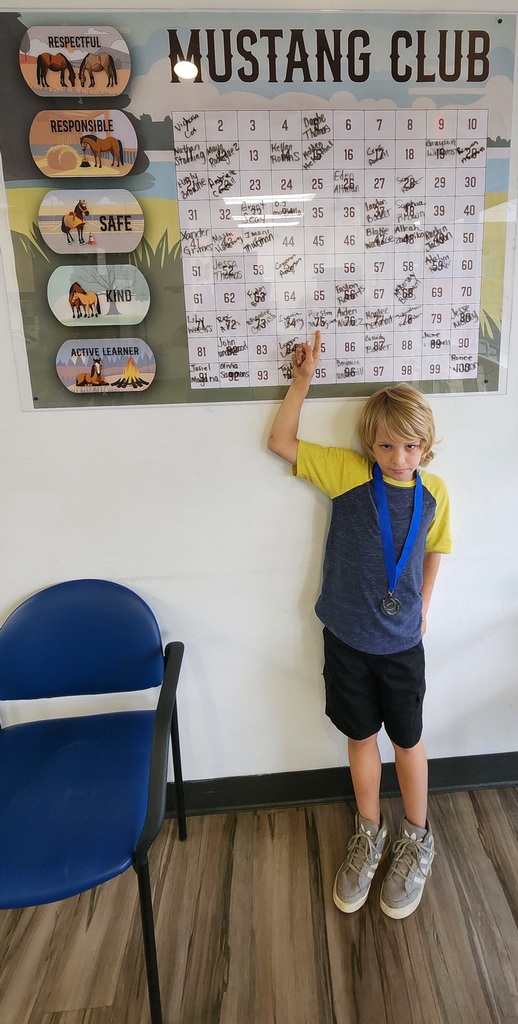 Picture of male student pointing at the Mustang Club board with his medal.