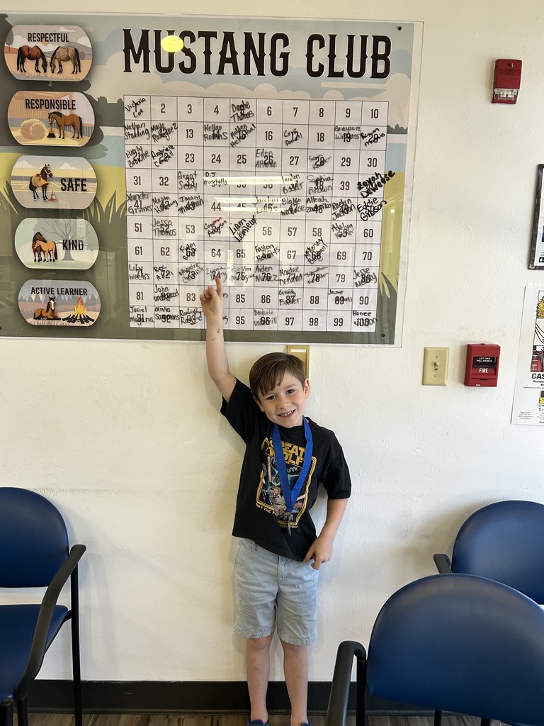 Picture of male student pointing at the Mustang Club board with his medal.