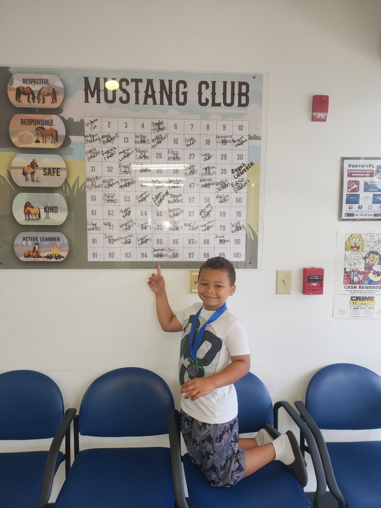 Picture of male student pointing at the Mustang Club board with his medal.