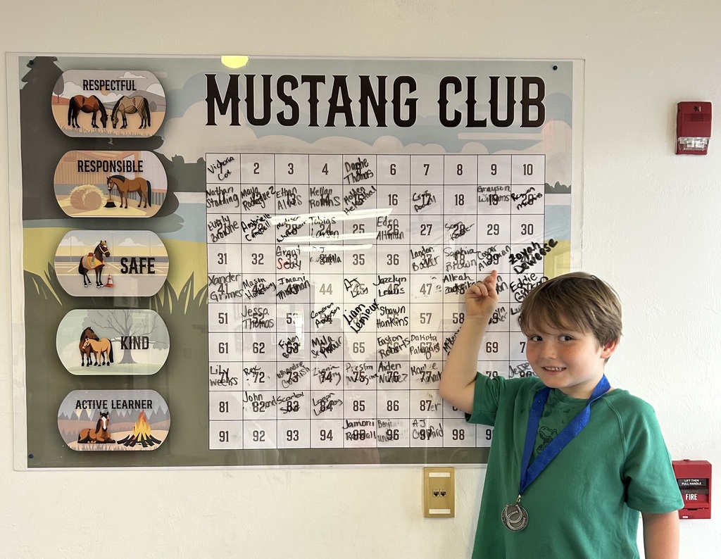Picture of male student pointing at the Mustang Club board with his medal.