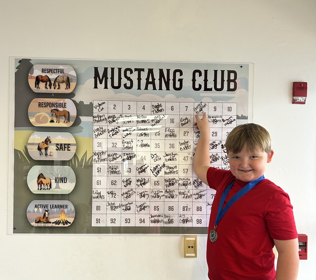 Picture of male student pointing at the Mustang Club board with his medal.
