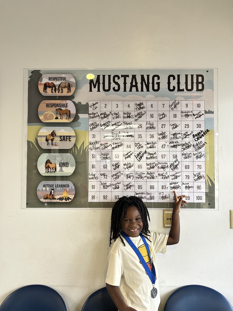 Picture of male student pointing at the Mustang Club board with his medal.