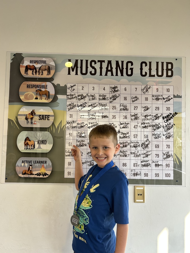 Picture of male student pointing at the Mustang Club board with his medal.