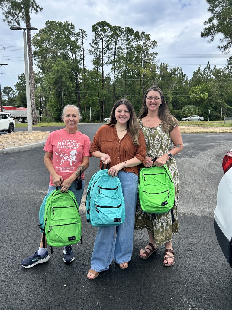 Picture of 3 Caucasian ladies holding bookbags standing in parking lot of Melrose Elementary.
