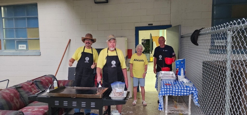 Picture of 3 men and one lady with a grill cooking pancakes.  They are wearing aprons with Kiwanis on them.