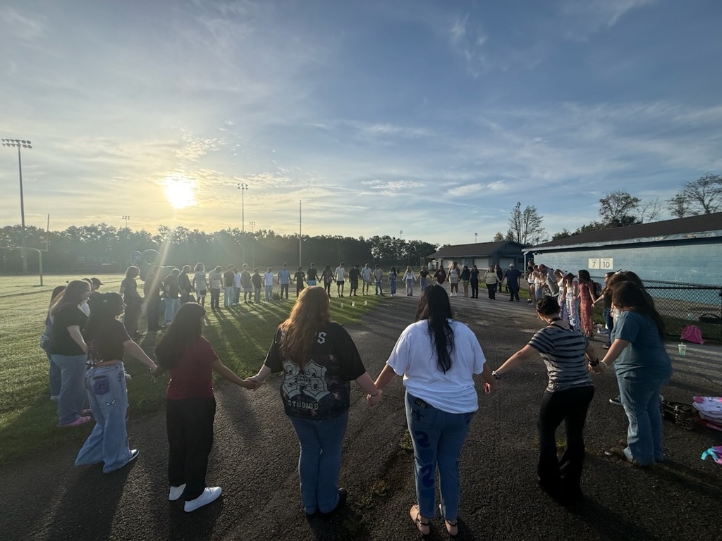 Students in a circle with the sun rising. 