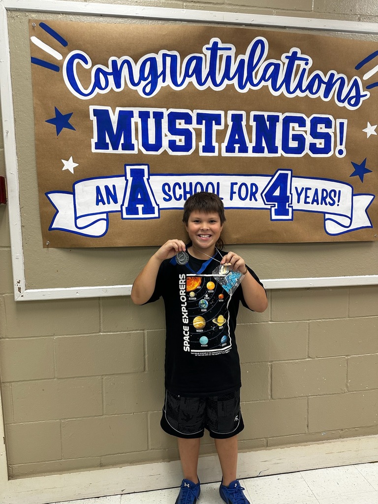 picture of male student in front of congratulations Mustangs sign holding his Mustang Club medal