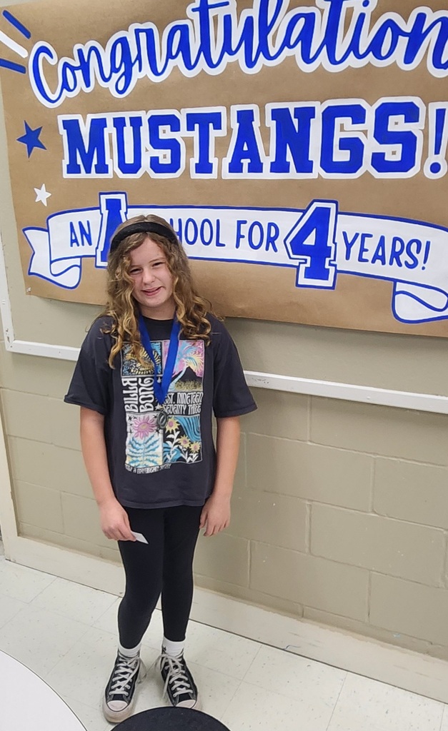 picture of female student in front of congratulations Mustangs sign holding her Mustang Club medal