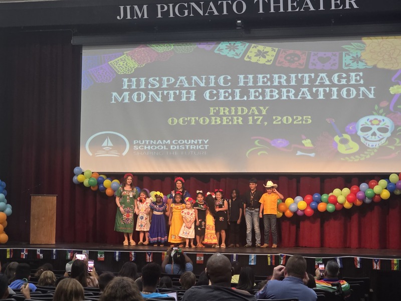 Picture of students on stage in front of screen that says Hispanic Heritage Month Celebration.