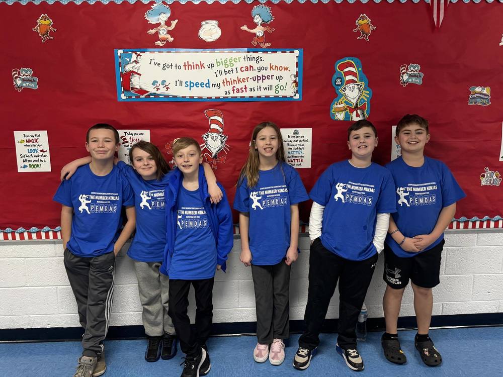 6 students standing with one another in front of a bulletin board, students are posing for a group picture to show excitement about getting ready to attend math field day.