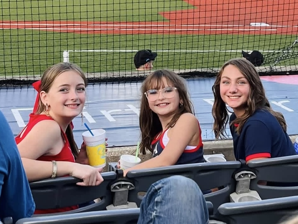 Three students sit in the chairs to watch the baseball game 