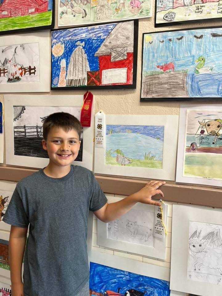Elementary student standing by art work.  4-H club winners