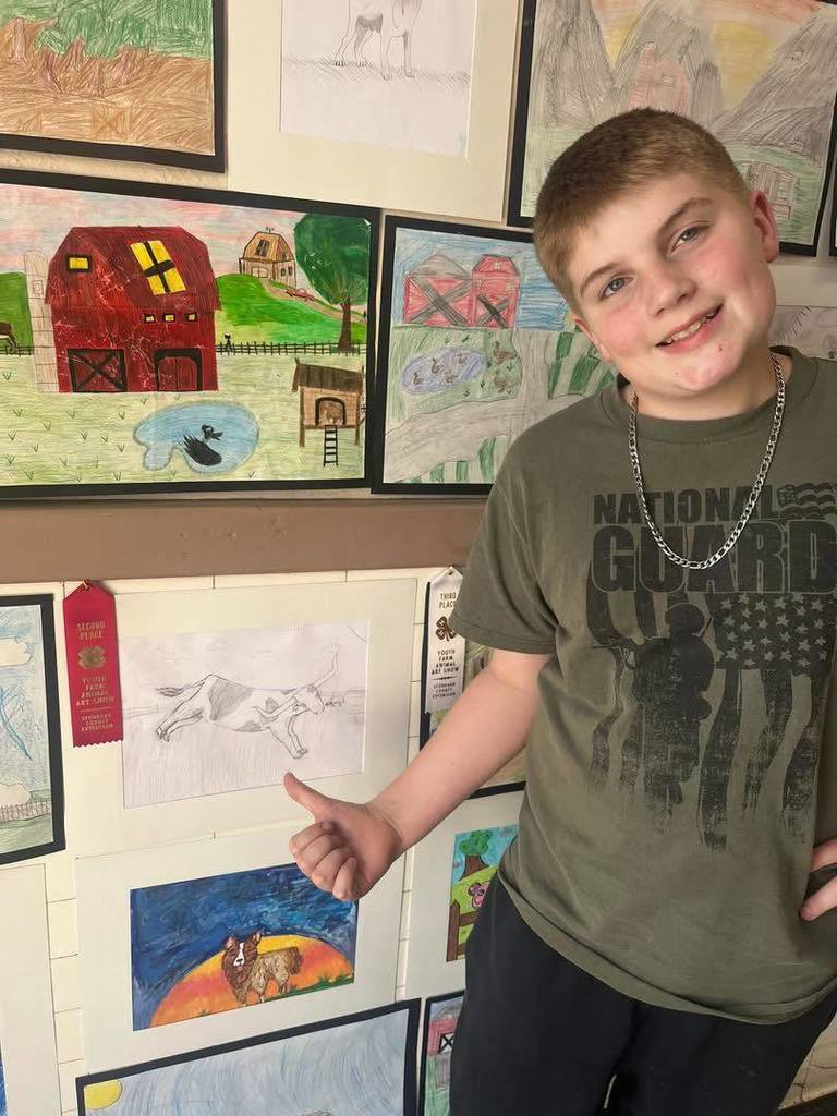 Elementary student standing by art work.  4-H club winners
