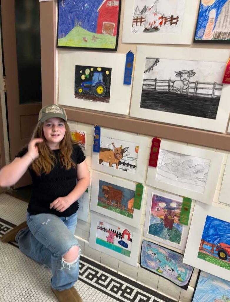 Elementary student standing by art work.  4-H club winners
