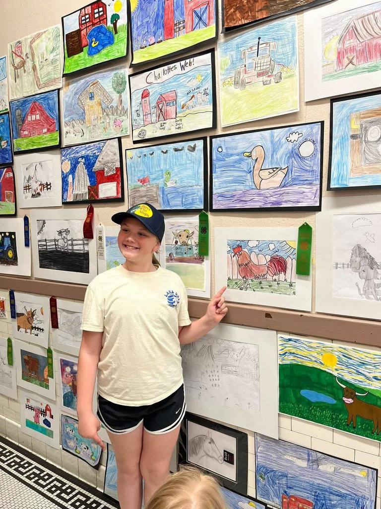 Elementary student standing by art work.  4-H club winners