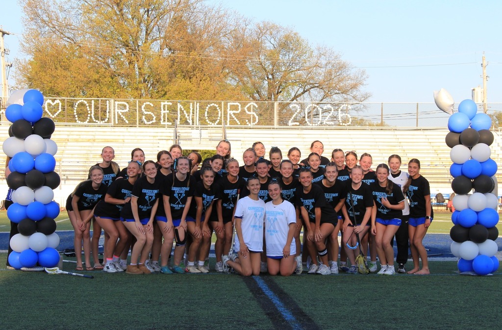 The entire girls lacrosse team smiling on the field.