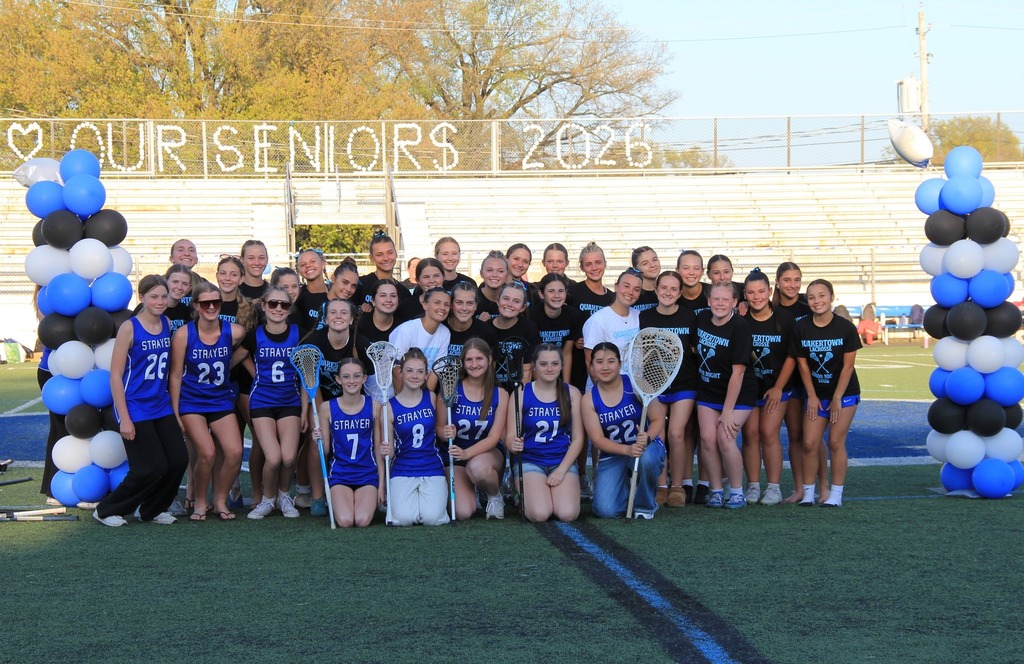 The entire girls lacrosse team, plus the middle school girls lacrosse team smiling on the field.