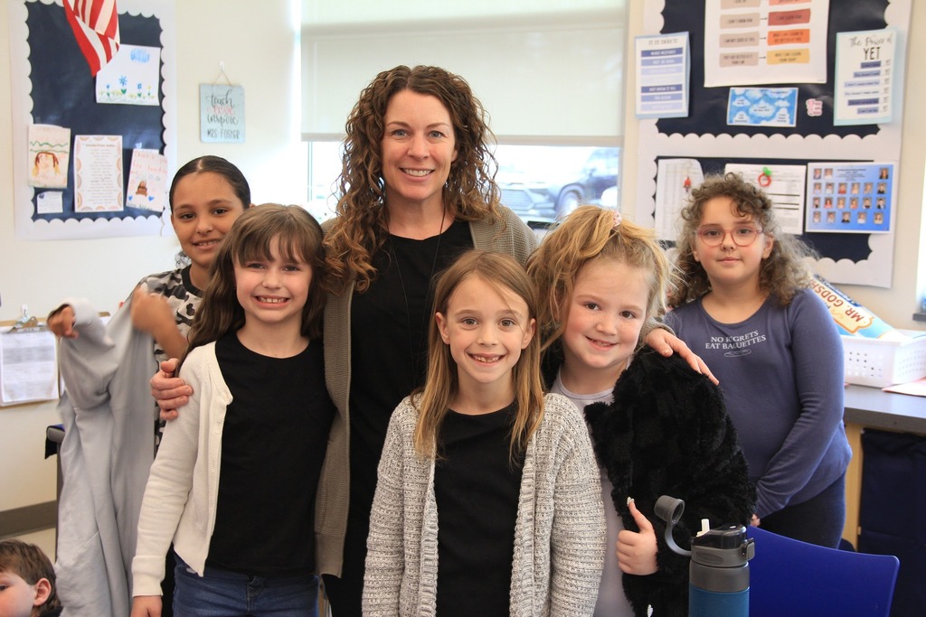 Students smile wearing black shirts and cardigans that match their teacher