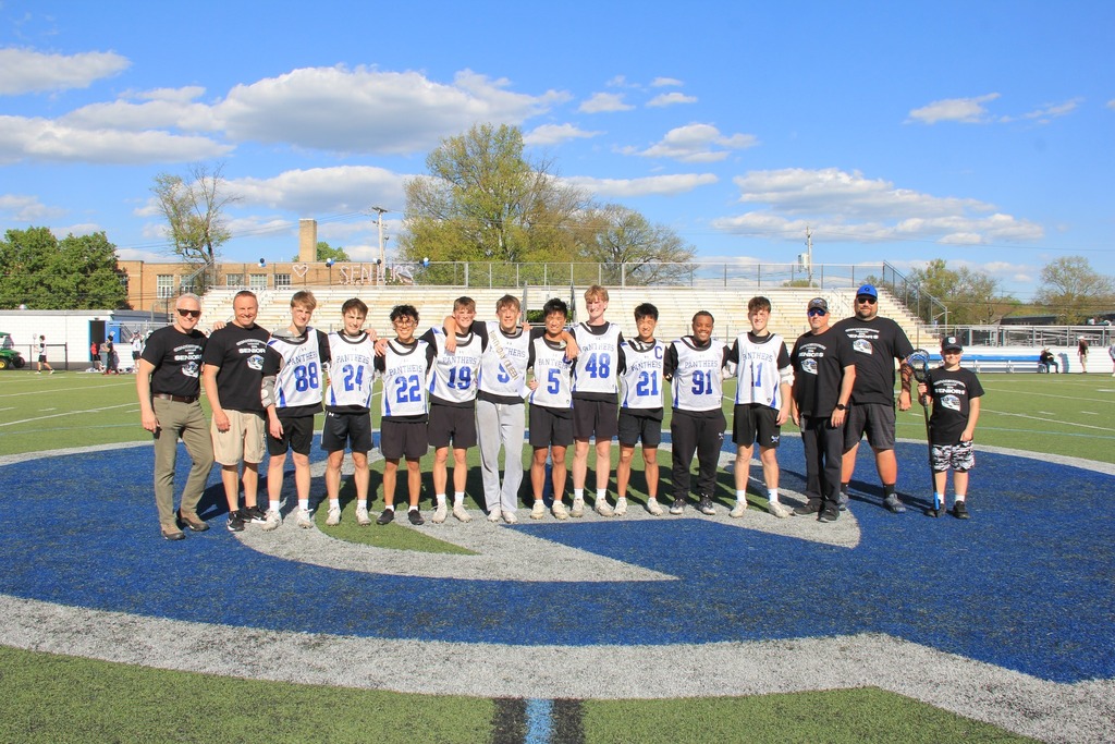Senior Boys Lacrosse players smile with their coaches on the field.