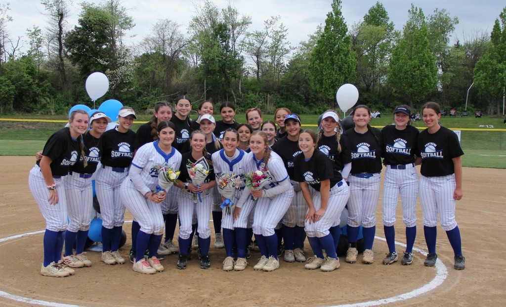 The entire softball team smiling on the pitchers mound.