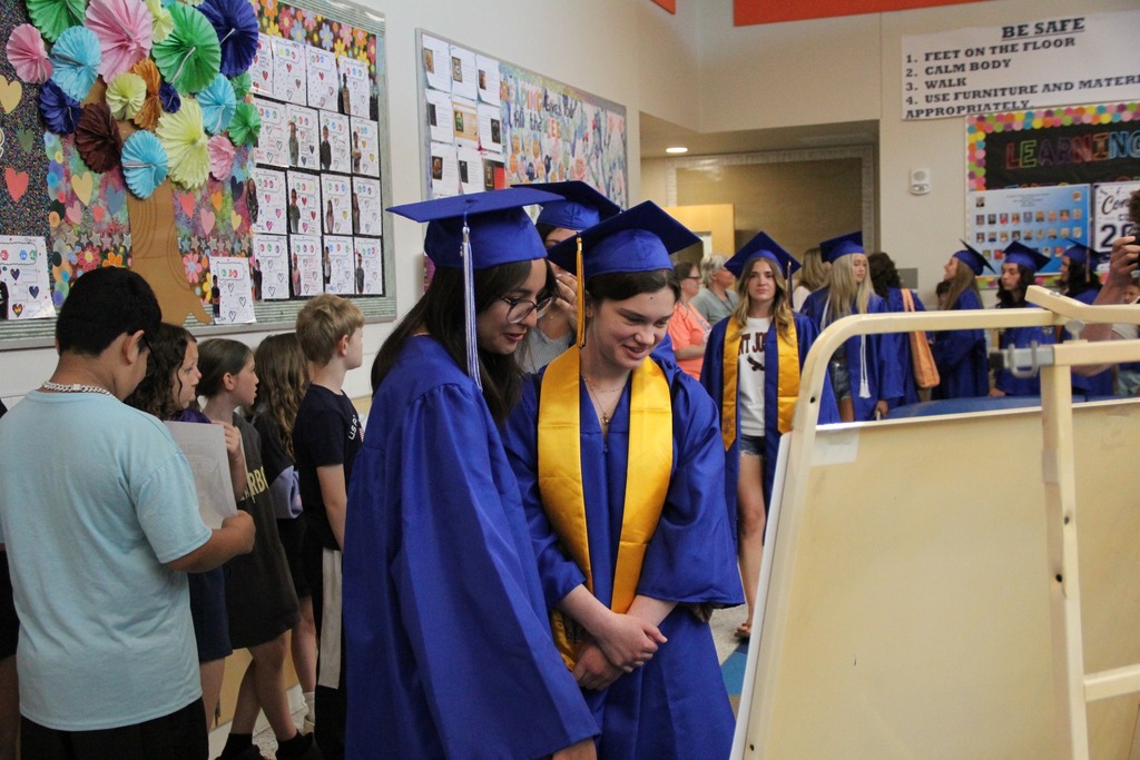Seniors in their caps and gowns view old photos of themselves in elementary school