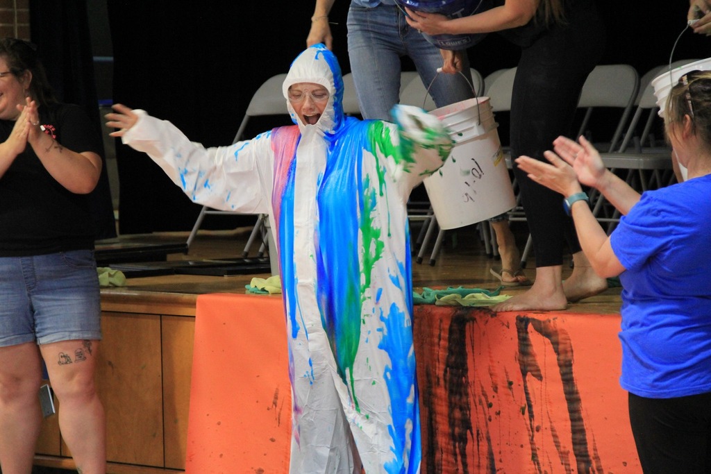 Dr. Z, standing in a baby pool and wearing a white coverall gets slimed from head to toe