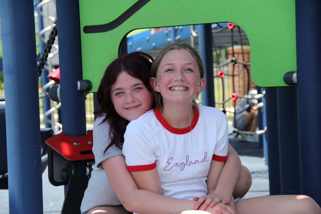 Two 5th grade girls smile for a photo on playgound equipment