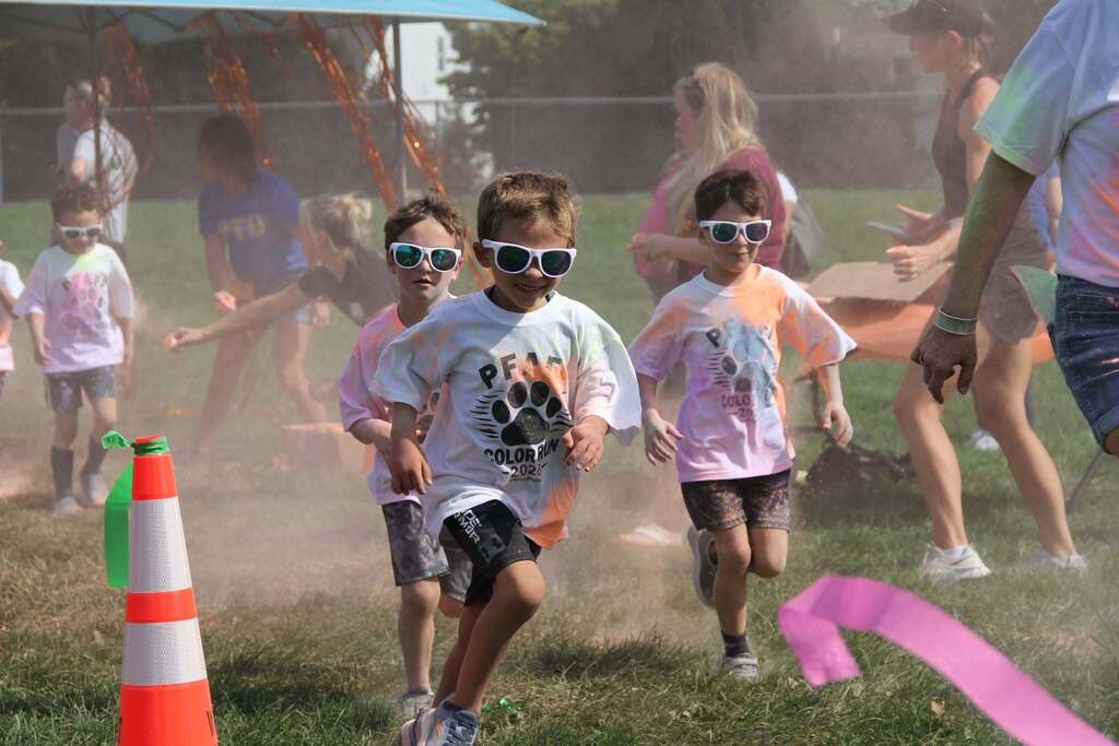 Children running through the grass and getting splashed with chalk color clouds