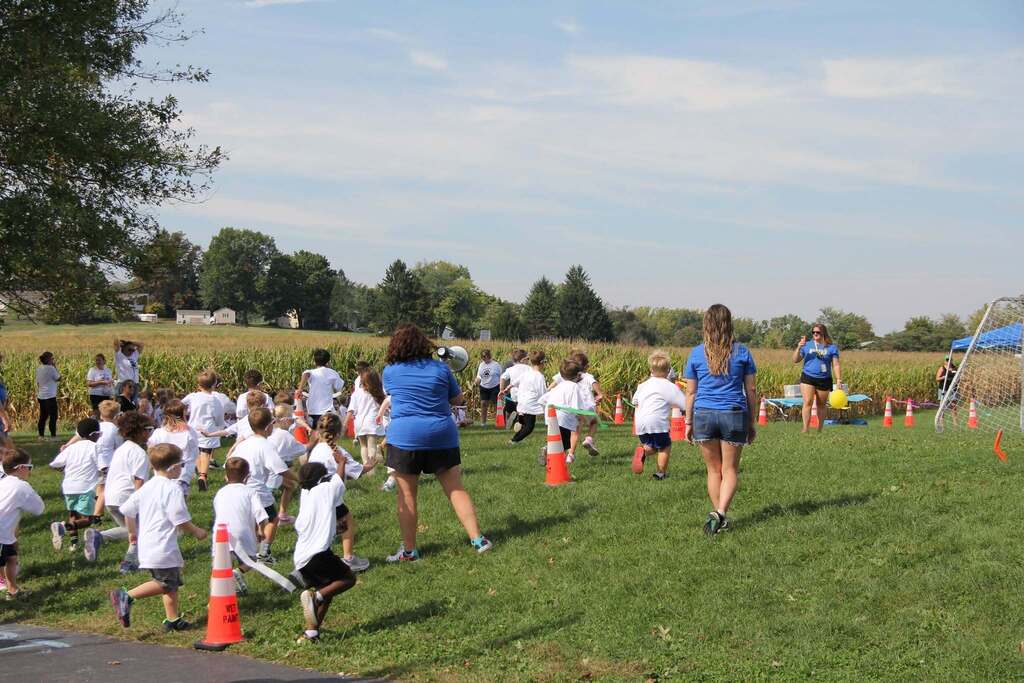 Children running up a grassy hill in white shirts