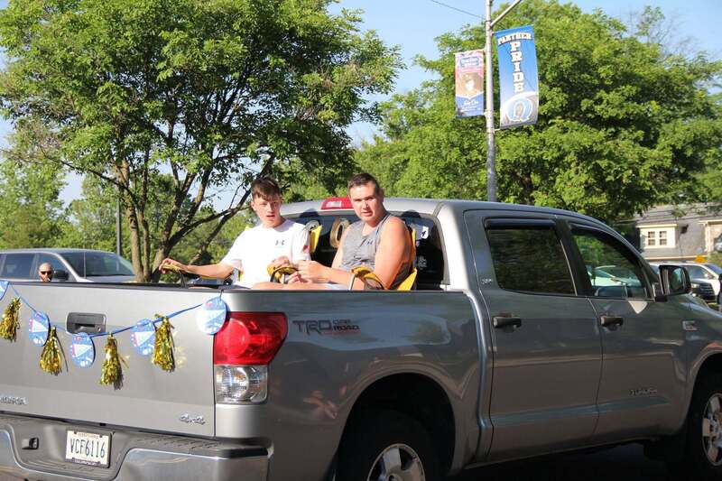 Students wave from the back of a pick up truck