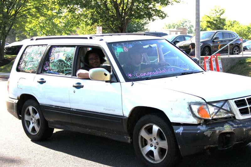 Student waves from the passenger side window of a white subaru forrester